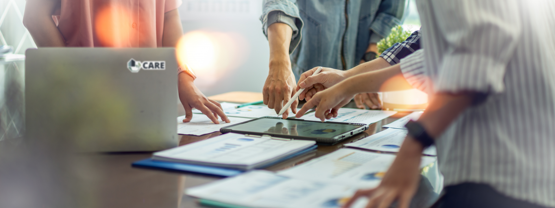 © Yingyaipumi, Adobe Stock Hands of several people working together over a desk with a tablet and sheets of diagrams.